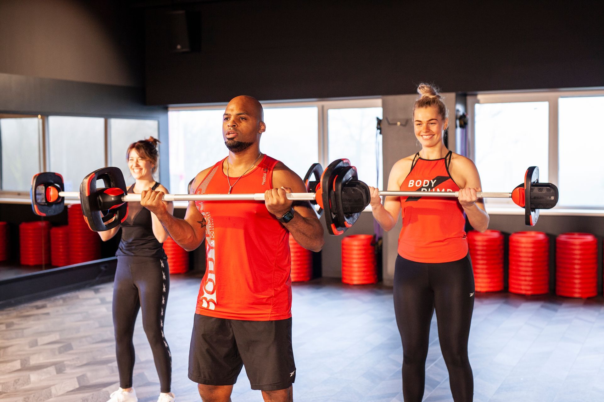 Een man en twee vrouwen tillen halters in een sportschool.