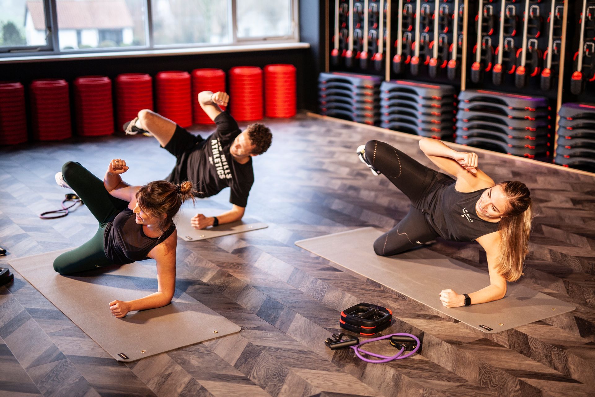 Drie mensen doen oefeningen op yogamatten in een sportschool.