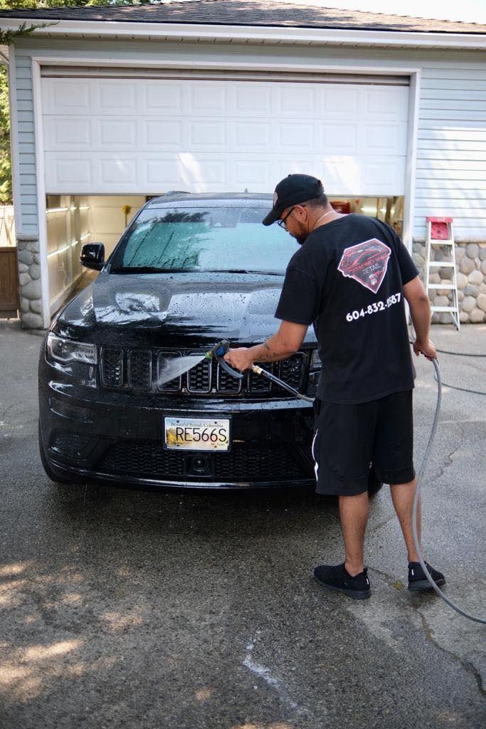 a man is washing a black jeep in front of a garage door .
