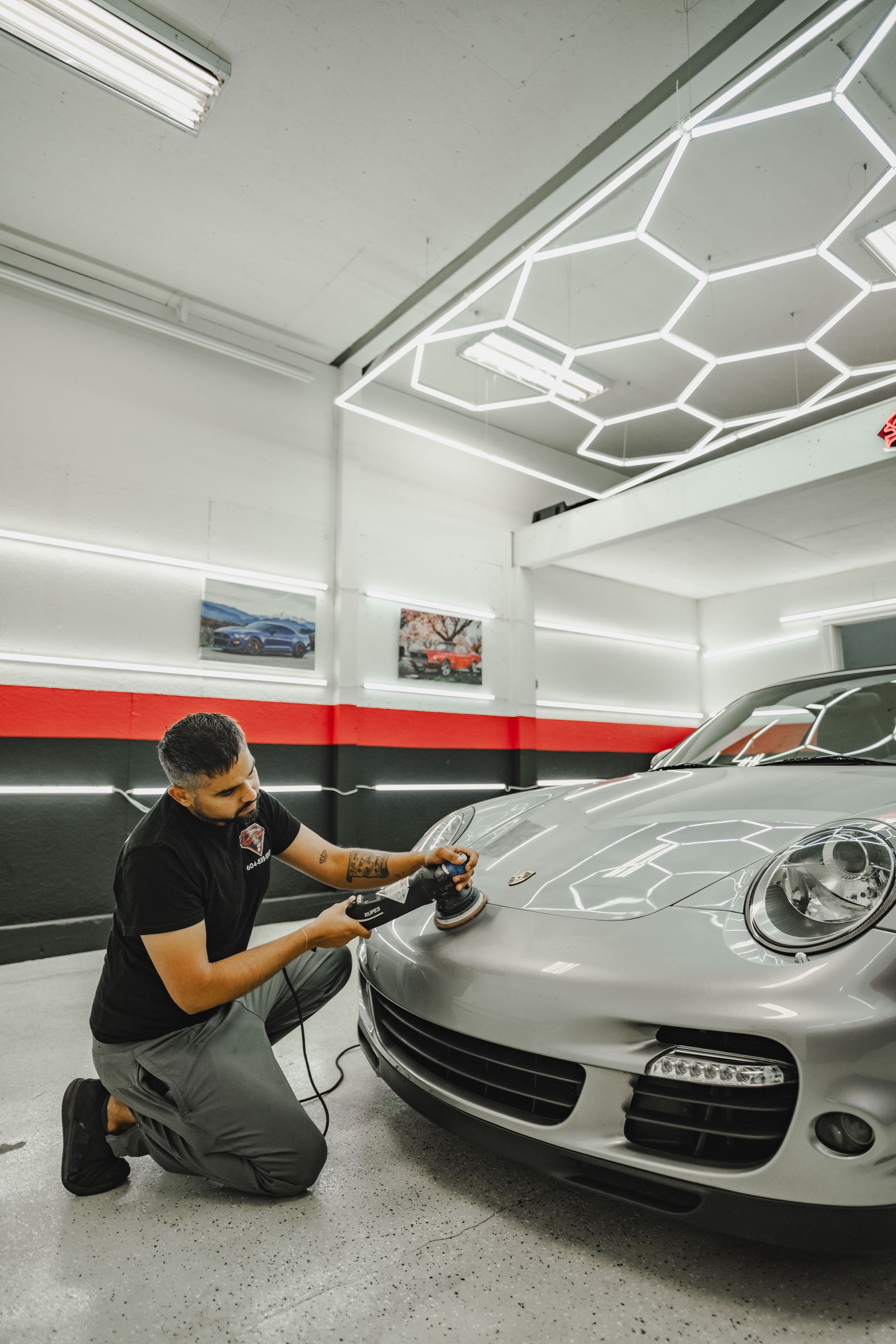 A person wearing black gloves is polishing the hood of a red car.