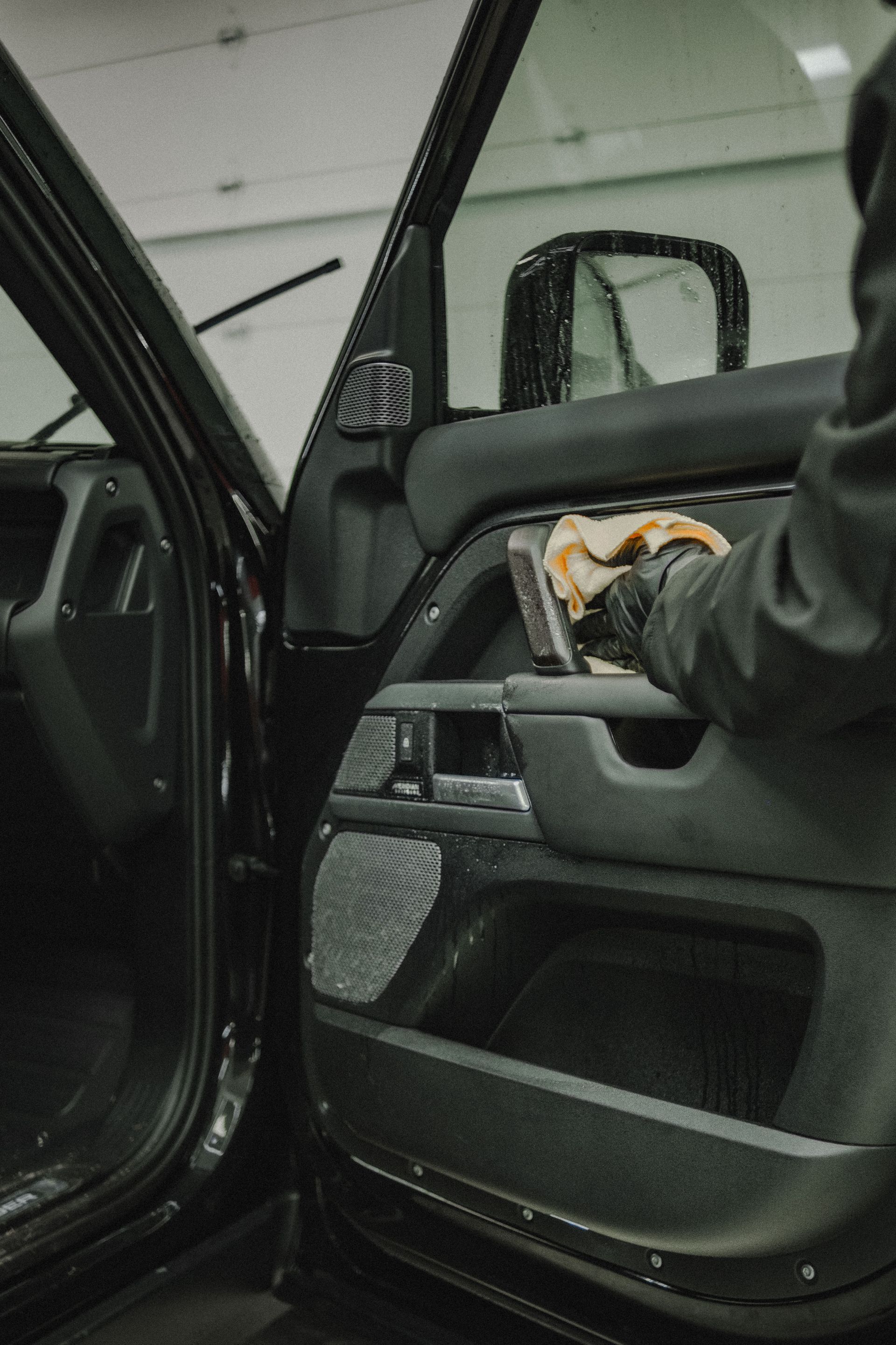Person cleaning a black car door panel with a brush.