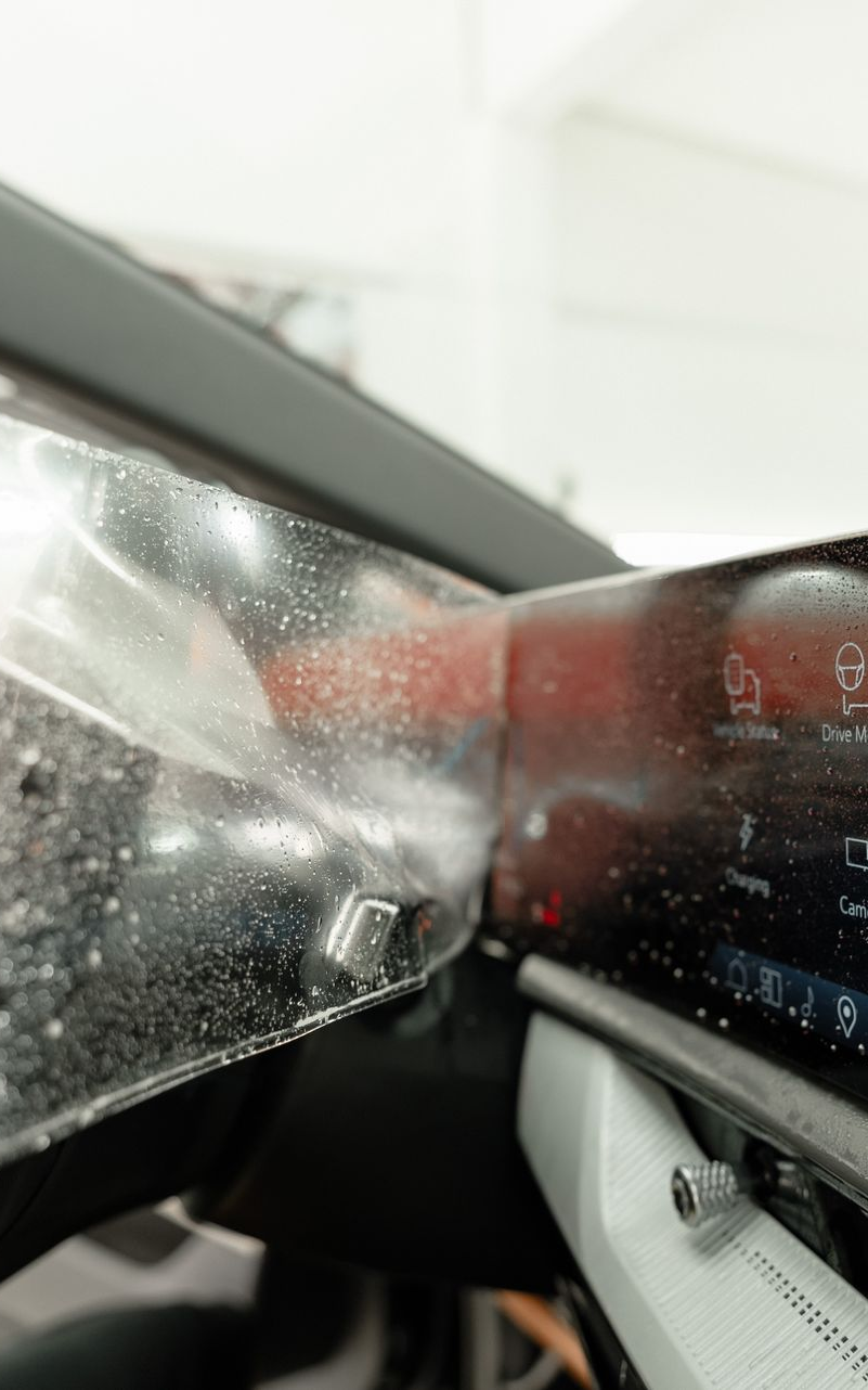 Applying a protective film to a car dashboard screen, showing the film being carefully smoothed.