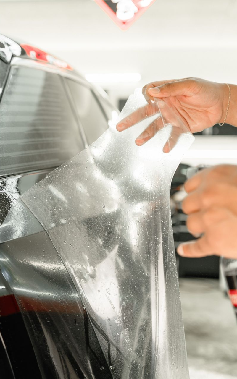 Person applying tinted film to a car window in a garage.