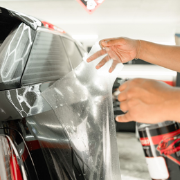 Person applying clear protective film to a car's taillight, indoors.
