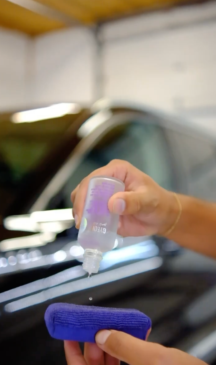 A person is holding a bottle of liquid in front of a car