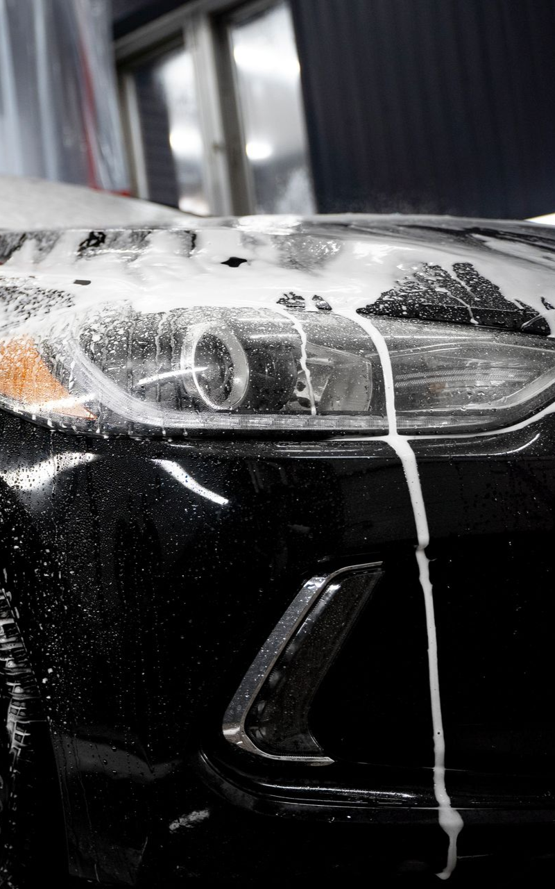 Black car headlight covered in white foam during a car wash.