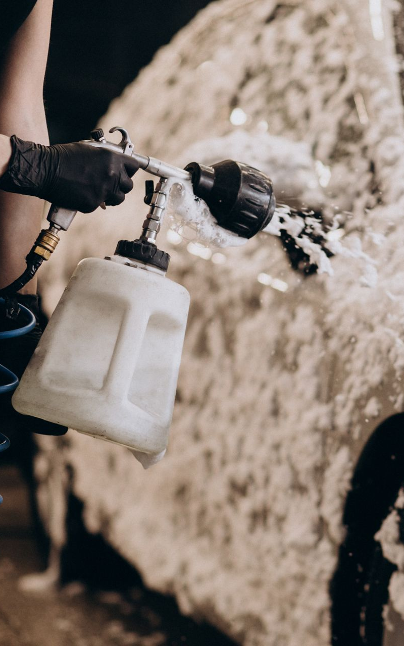 Person with black gloves spraying foam onto a car with a foam cannon.