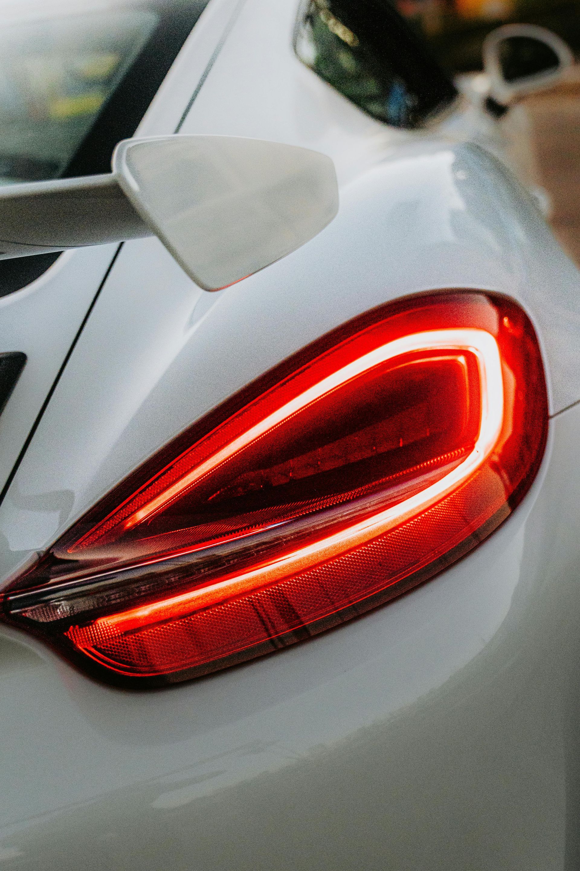 Red taillight on a white car, glowing against a light background.
