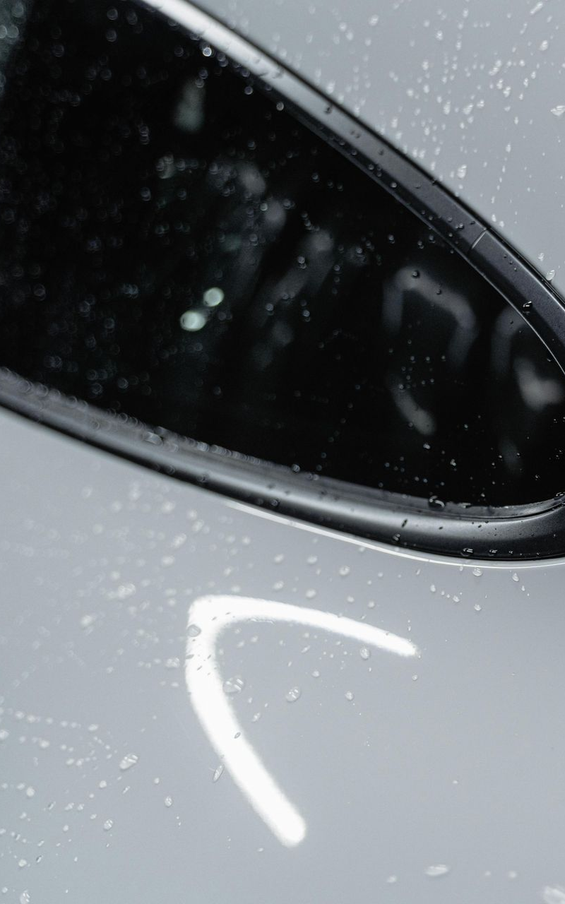 Black car mirror reflecting a curved light streak on a wet, white surface.