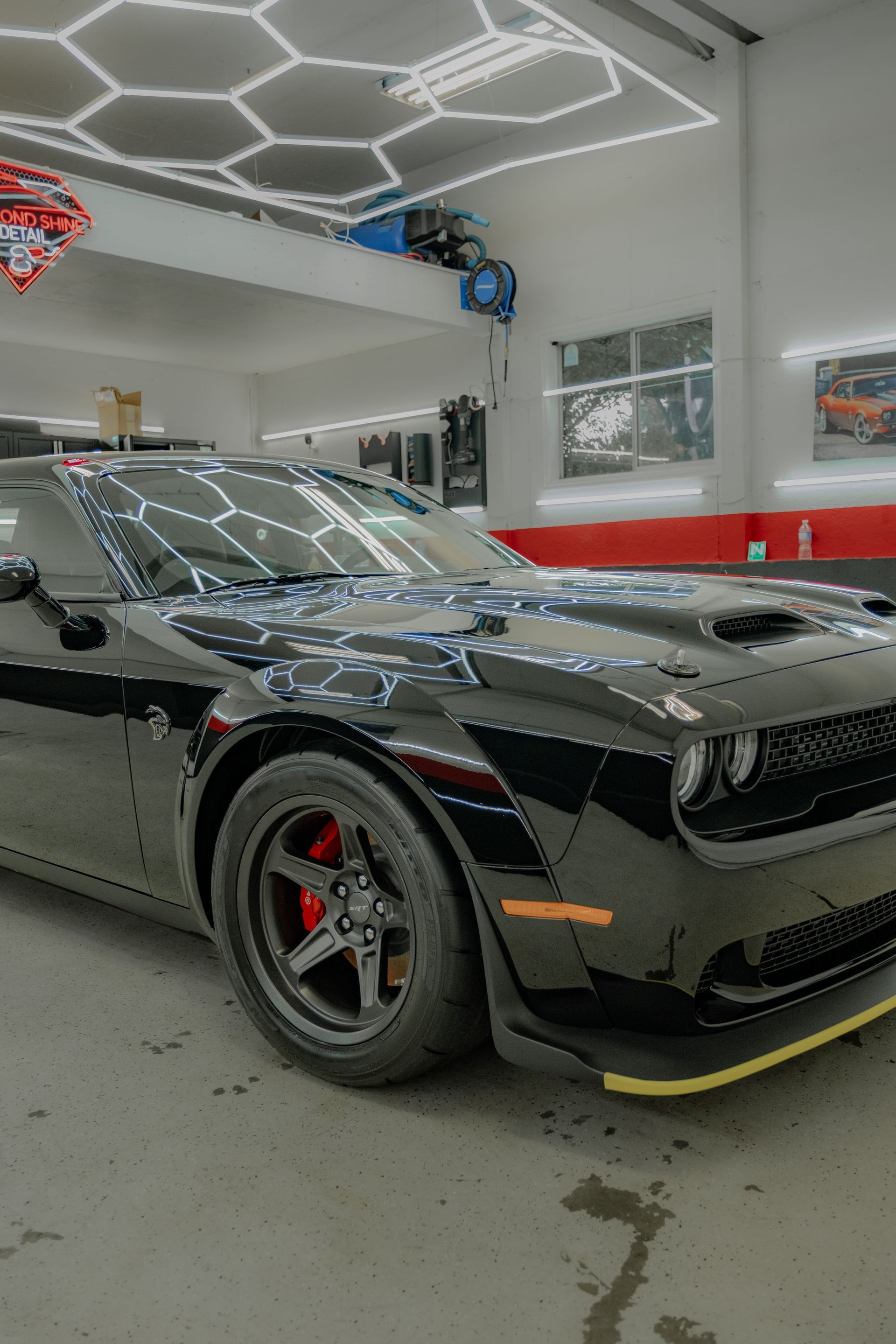 Black Dodge Challenger with red brake calipers in a well-lit auto shop.