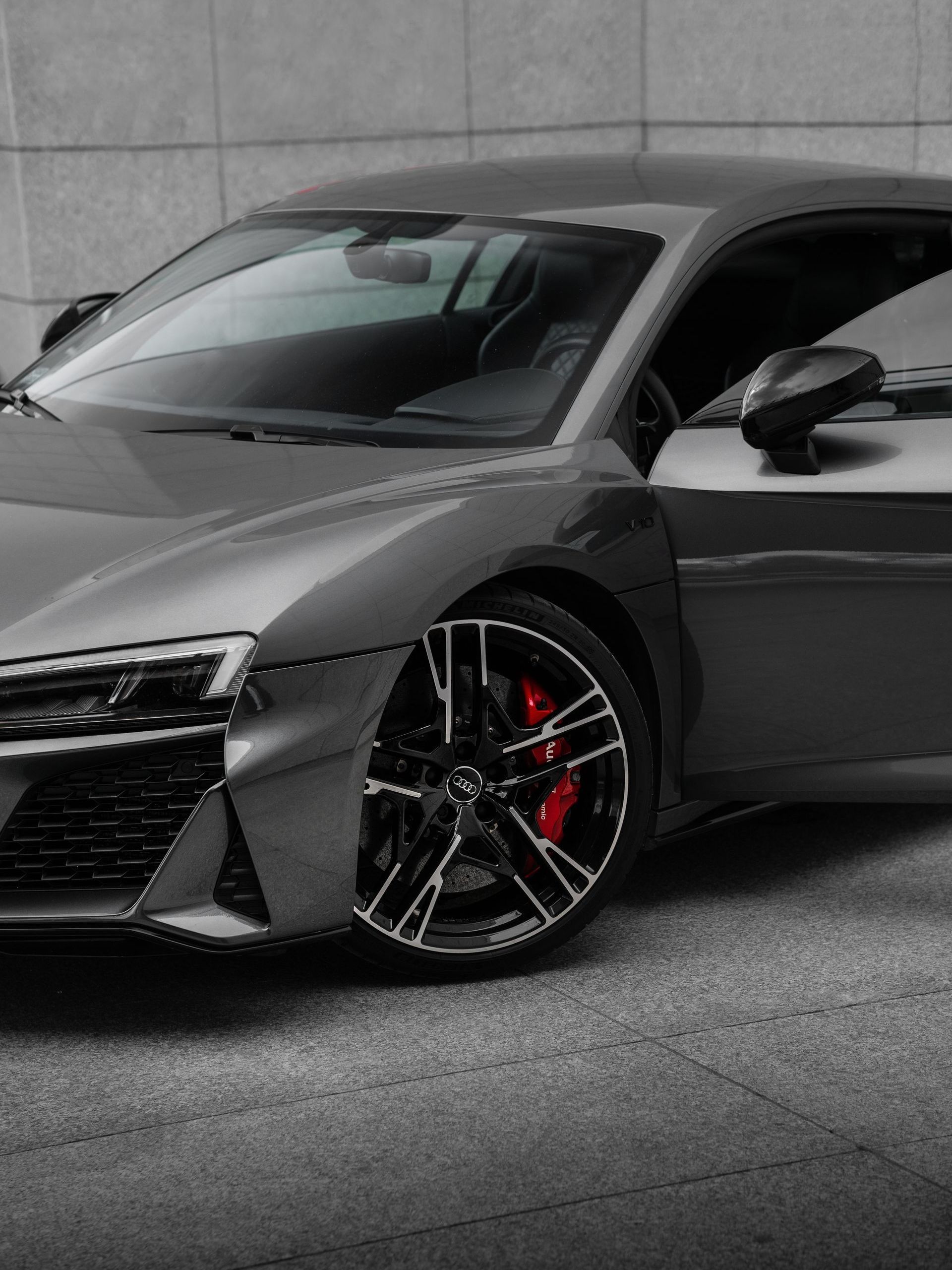 Gray Audi sports car, door open, parked on a gray surface. Black rims, red brake calipers.