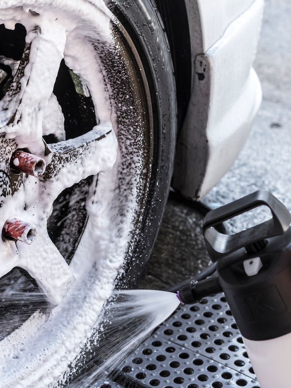 Washing a car wheel with foamy soap, nozzle spraying close up.