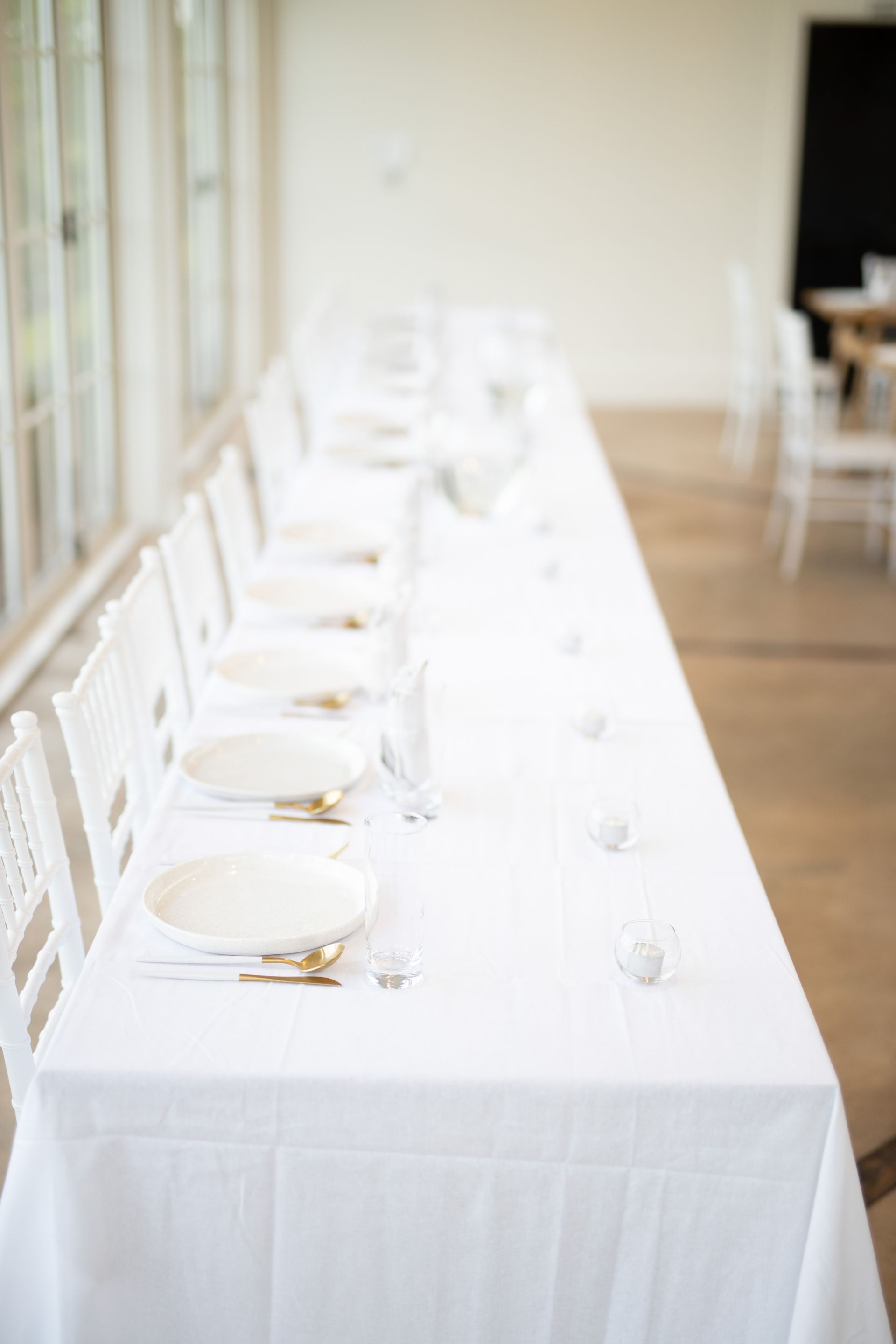 A long white table with plates , silverware , and candles on it.