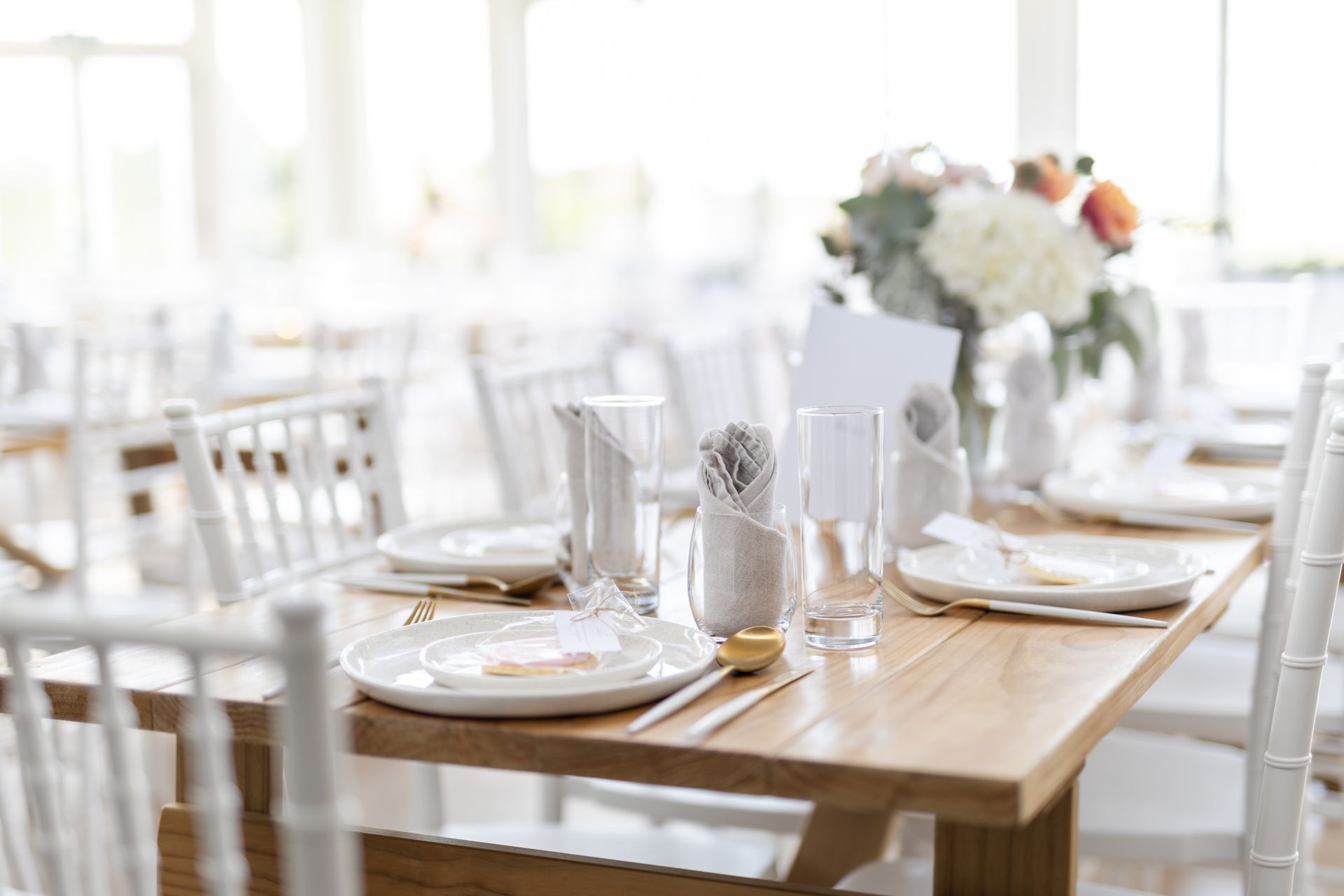 A wooden table with white chairs and plates and glasses on it.