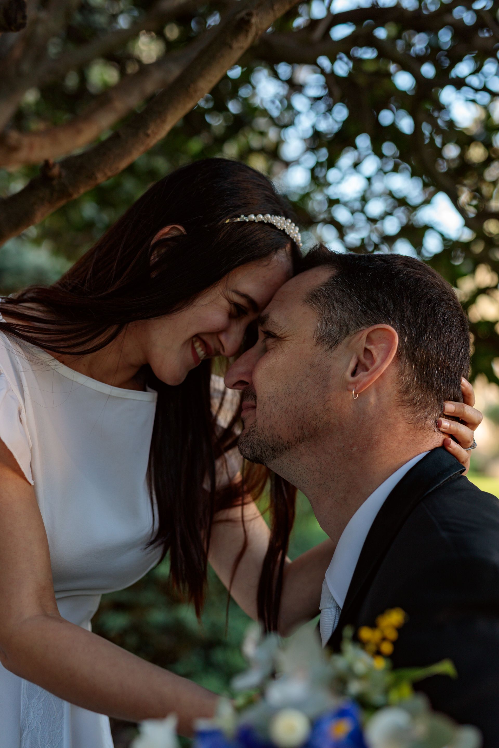 A bride and groom are kissing under a tree.