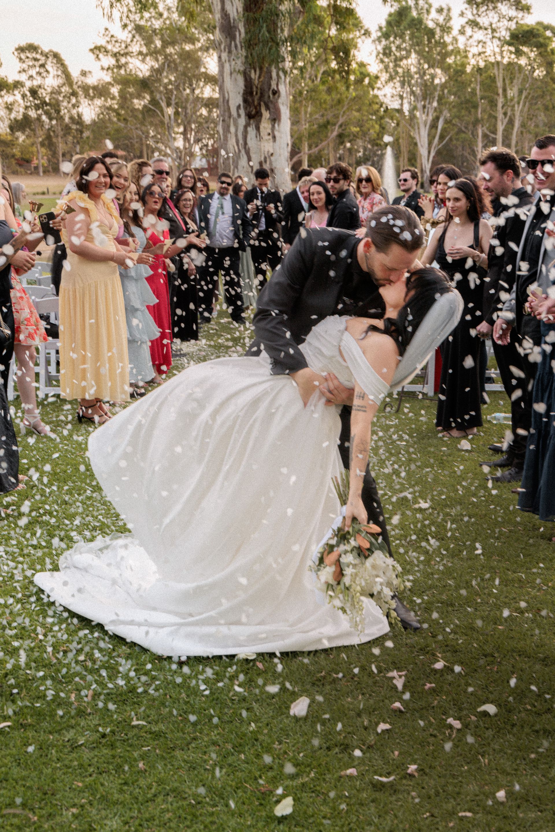 A bride and groom kissing in front of a crowd of people at their wedding.