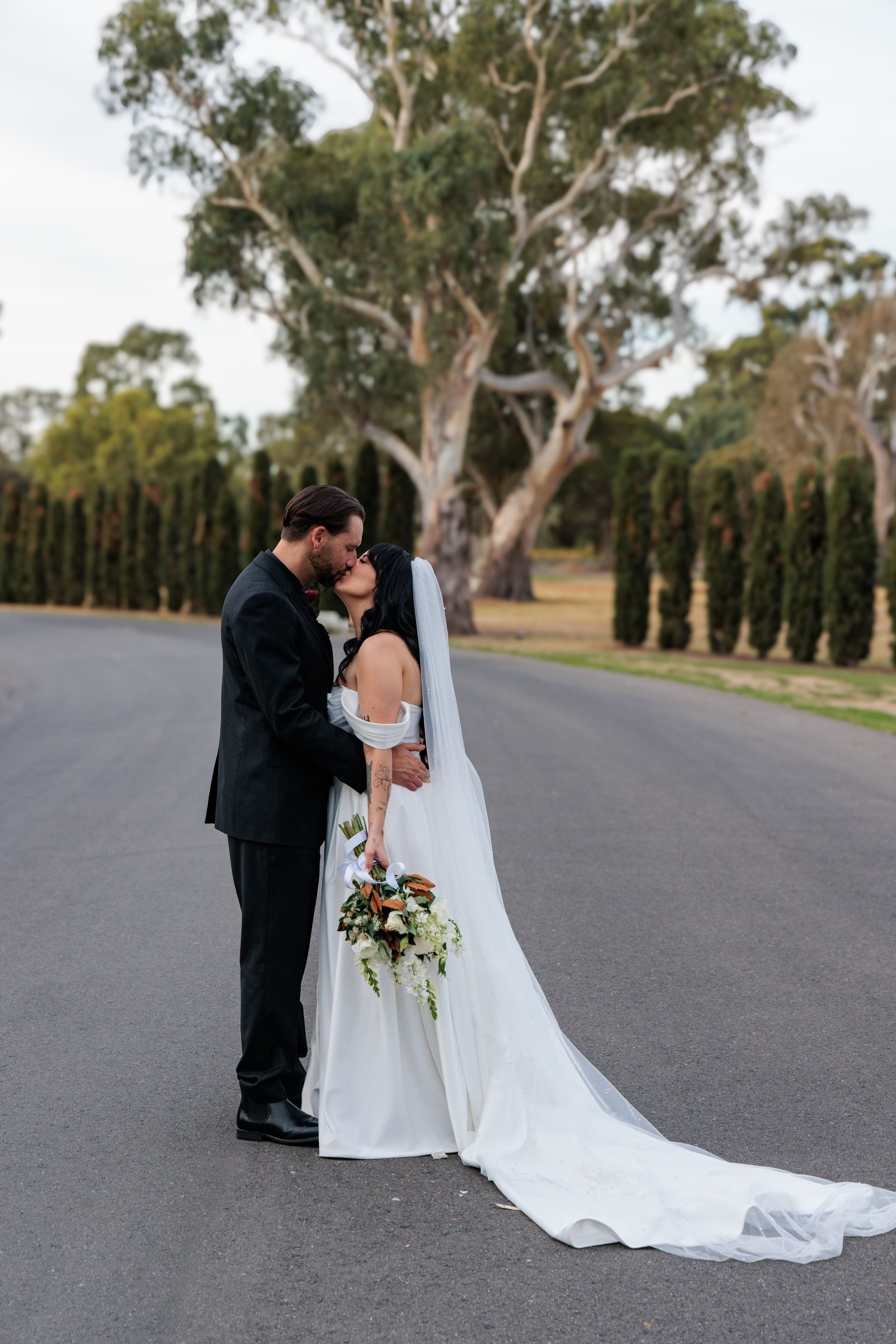 A bride and groom are kissing on the side of a road.