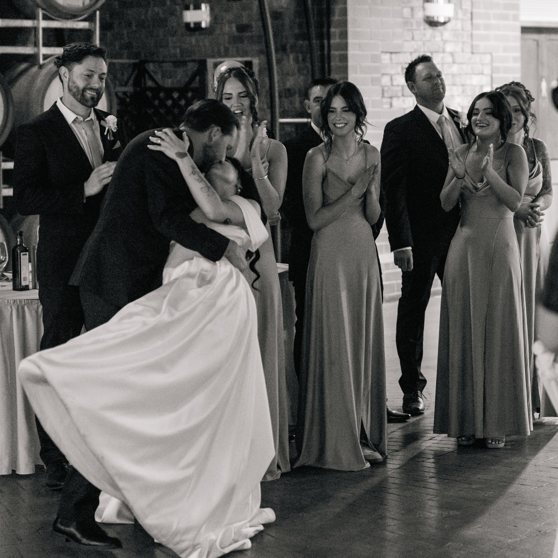 A bride and groom are kissing in front of their wedding party