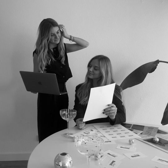 Twee vrouwen zitten aan een tafel en één houdt een stuk papier vast