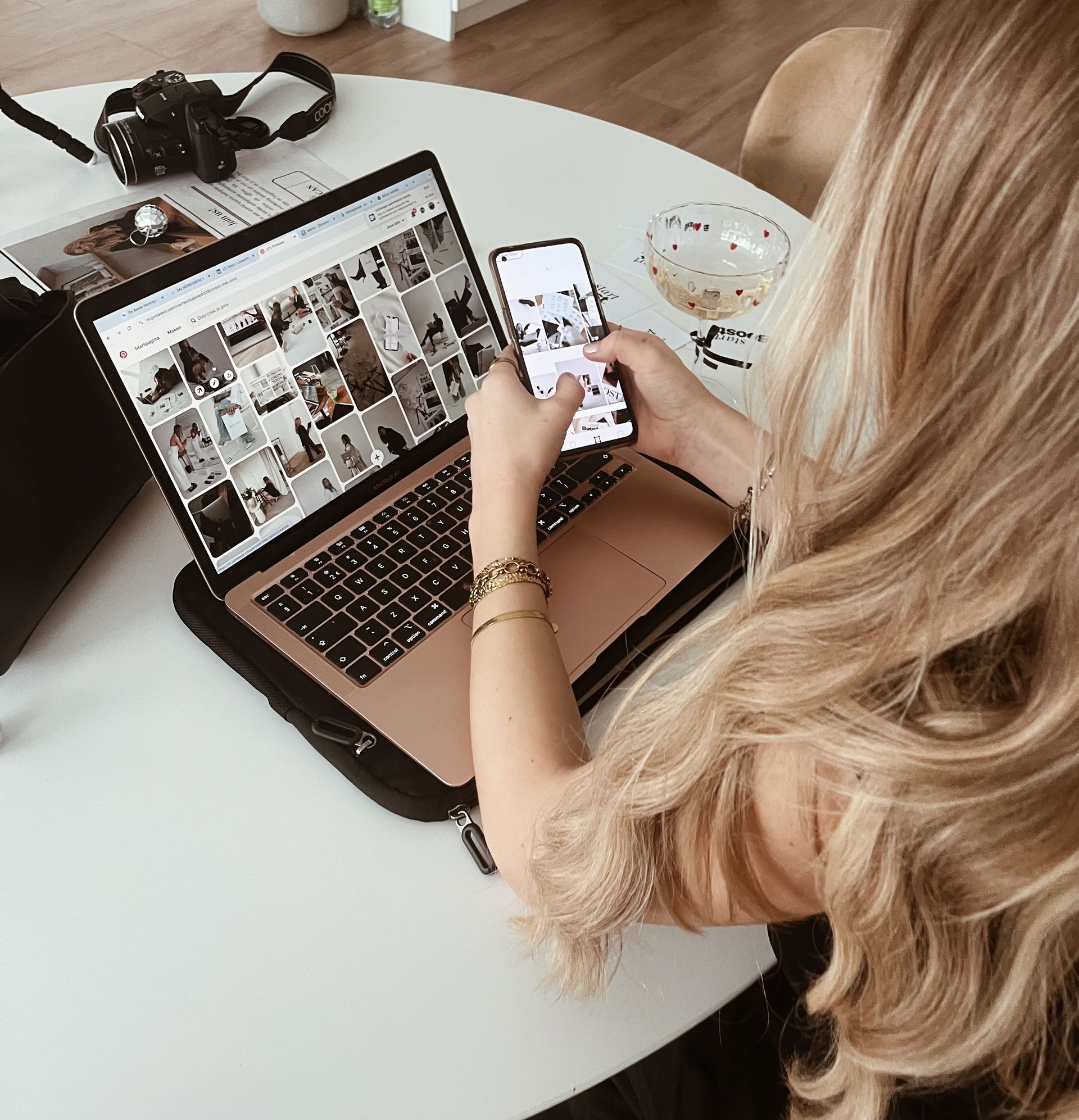 Een vrouw zit aan een tafel met een laptop en een mobiele telefoon