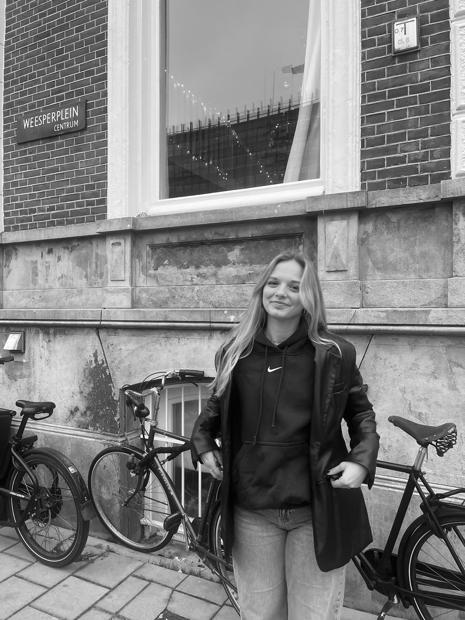 Een vrouw staat voor een gebouw naast een fiets.