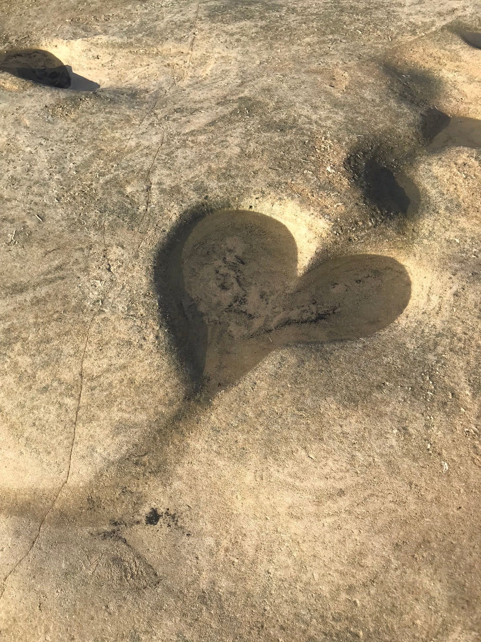 Een hartvormige schaduw in het zand op een strand.