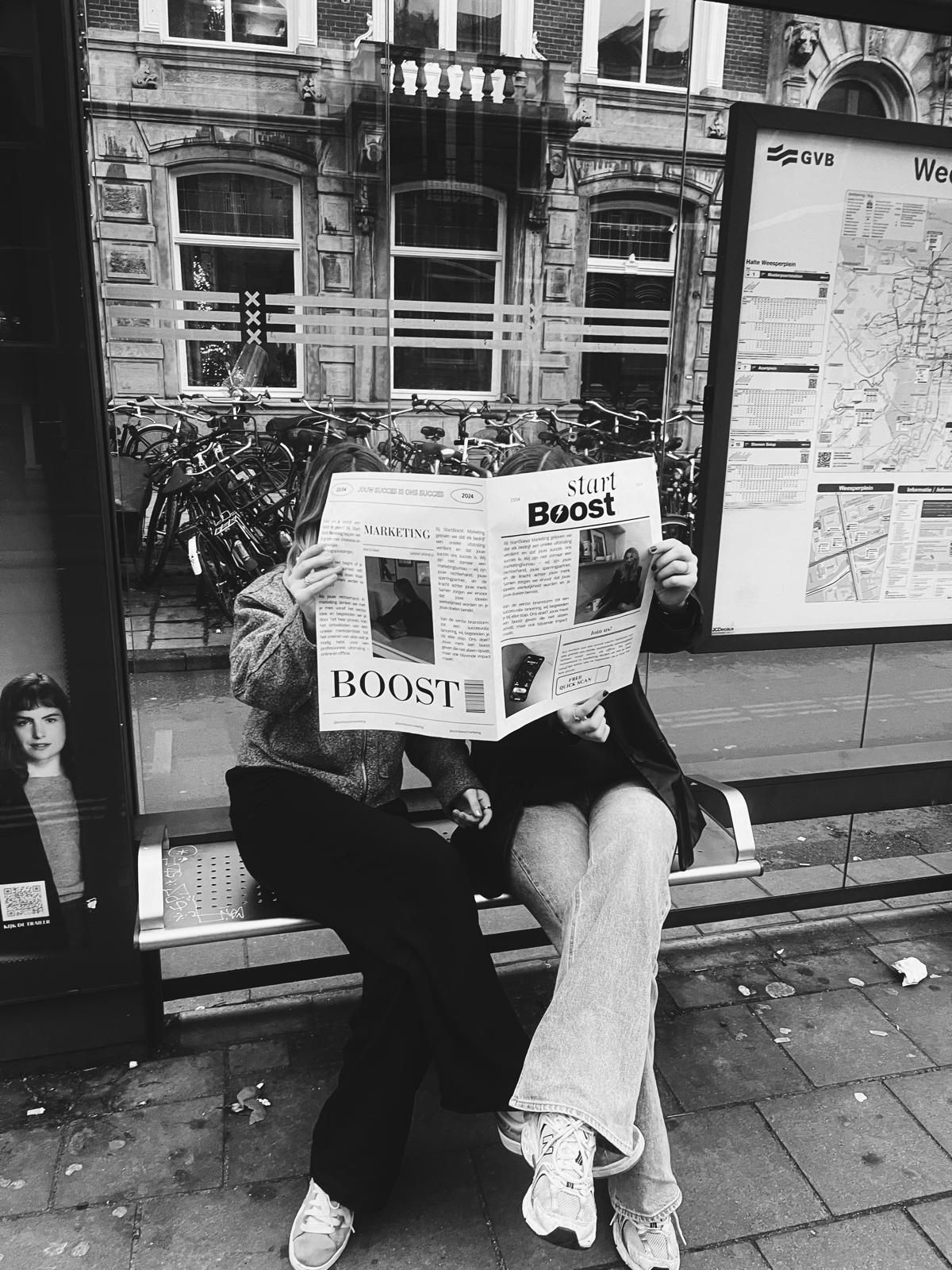Twee mensen zitten bij een bushalte en lezen een krant.