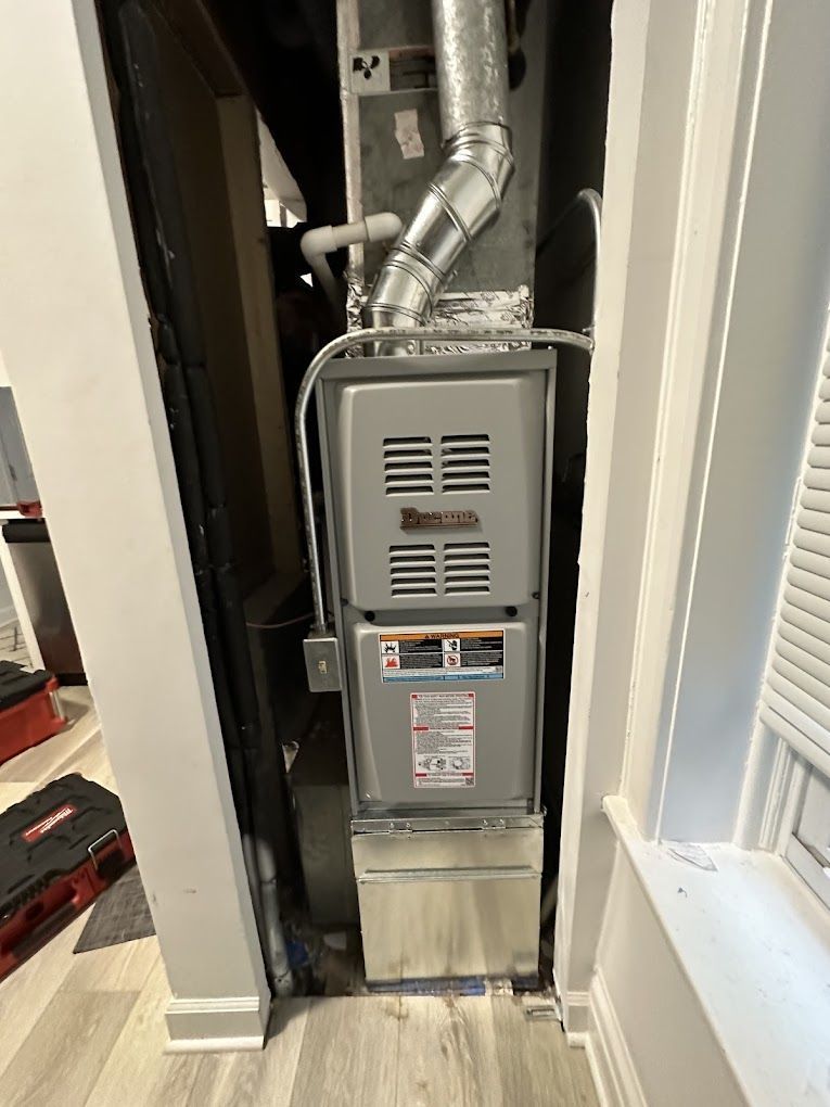 A furnace is sitting in the corner of a room next to a window.