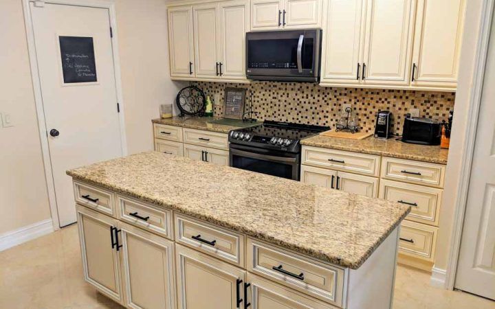 A kitchen with white cabinets , granite counter tops , a stove and a microwave.