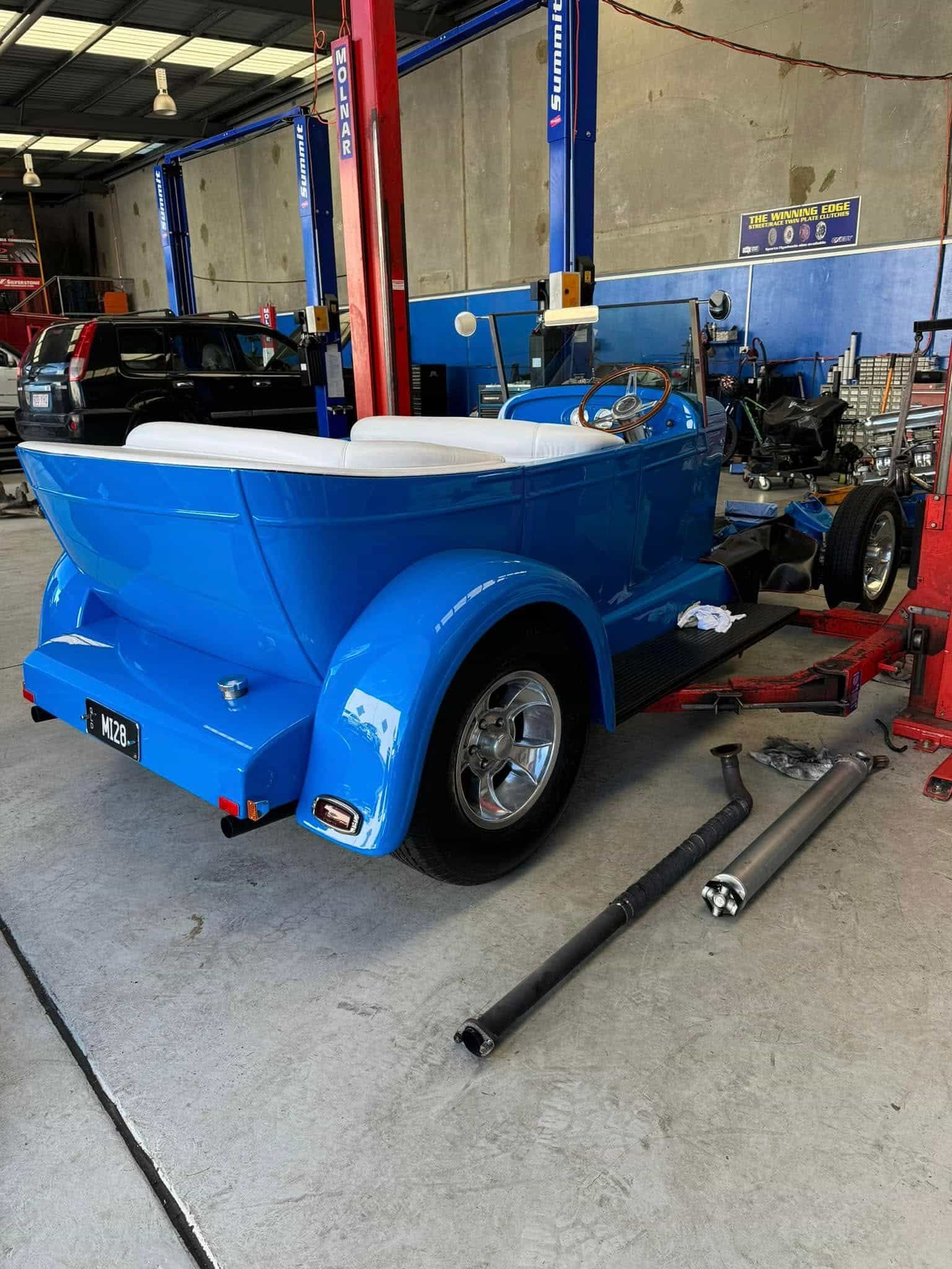 Blue hot rod in a garage, partially assembled. Chrome wheels, exhaust pipes on the floor — Pialba Brake Clutch & Steering in Pialba, QLD