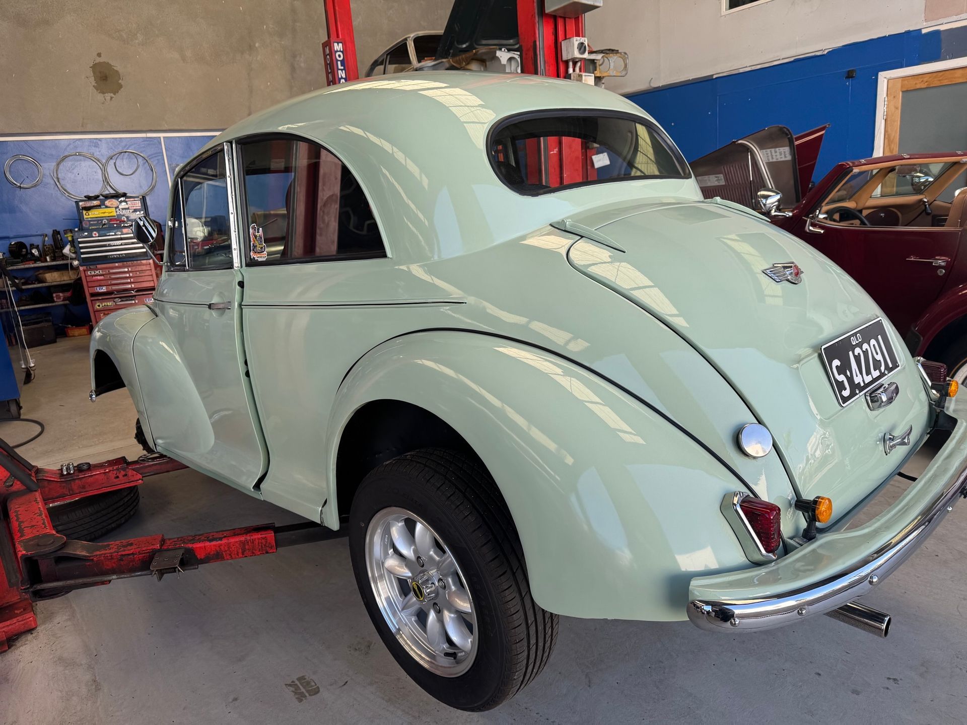 Light green classic car in a garage, partially raised on a lift.