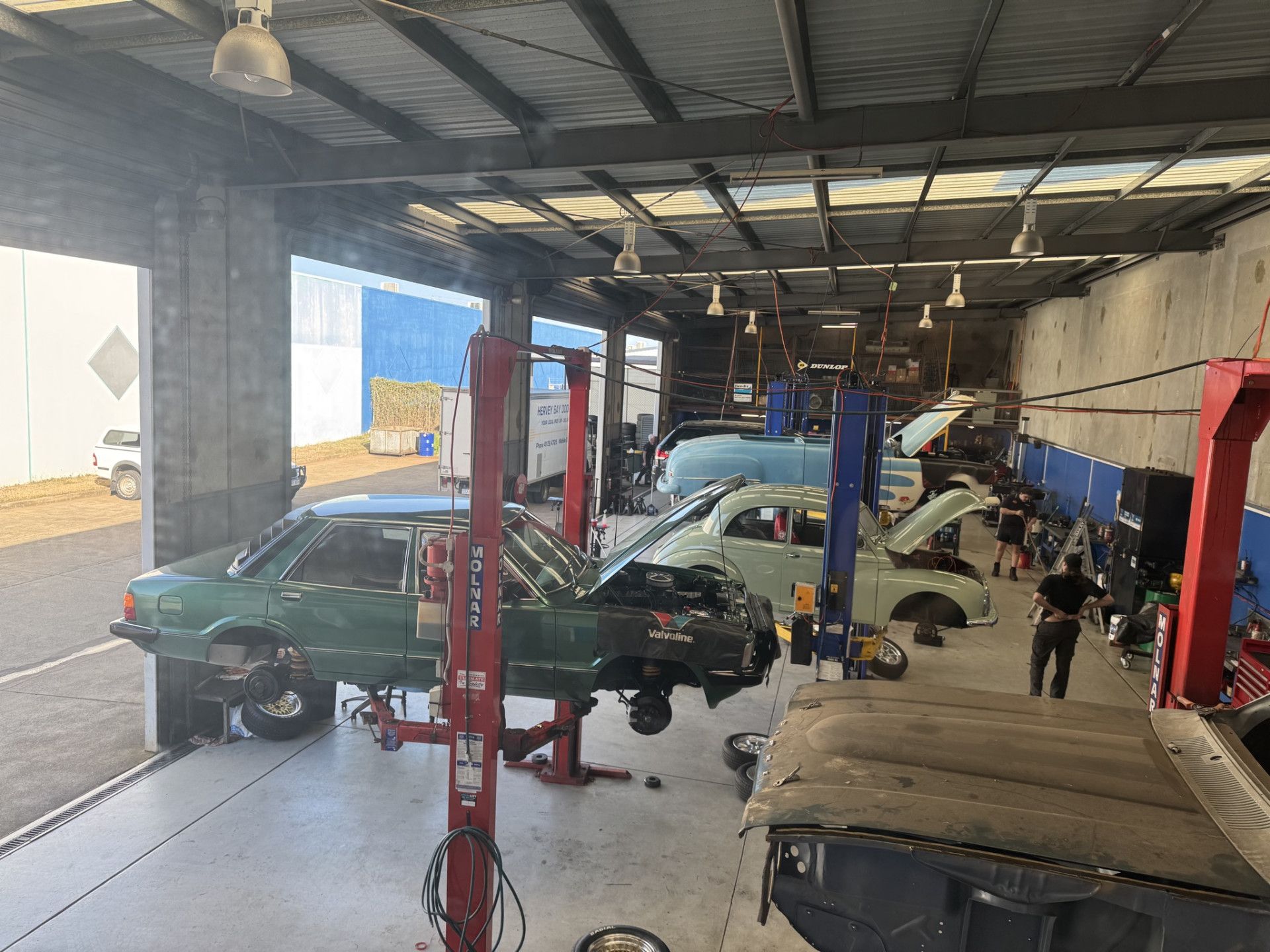 A car repair shop with several cars on lifts, mechanics working, and tools visible.