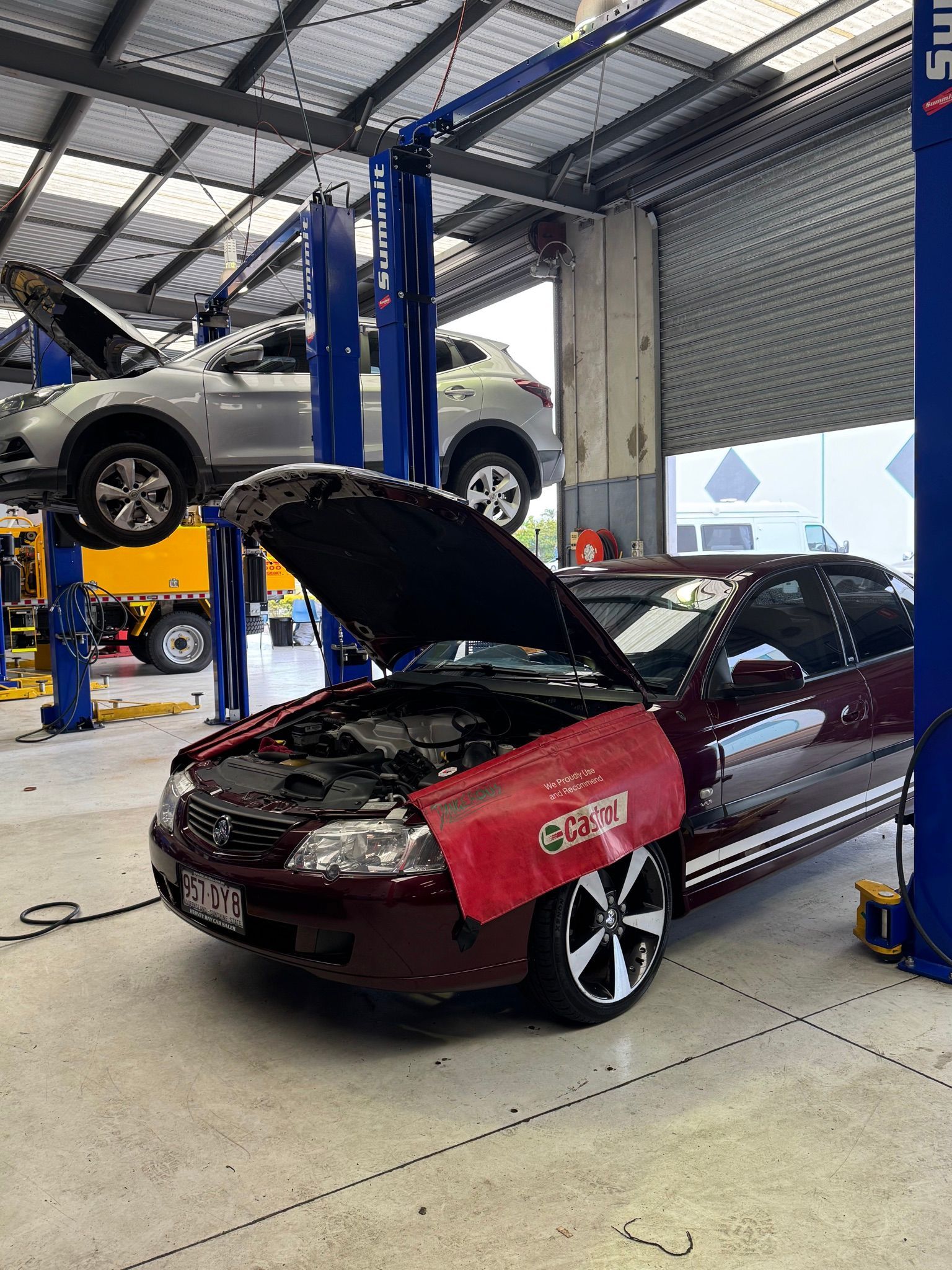 A maroon car with open hood in a garage, a car raised on a lift in the background — Pialba Brake Clutch & Steering in Pialba, QLD