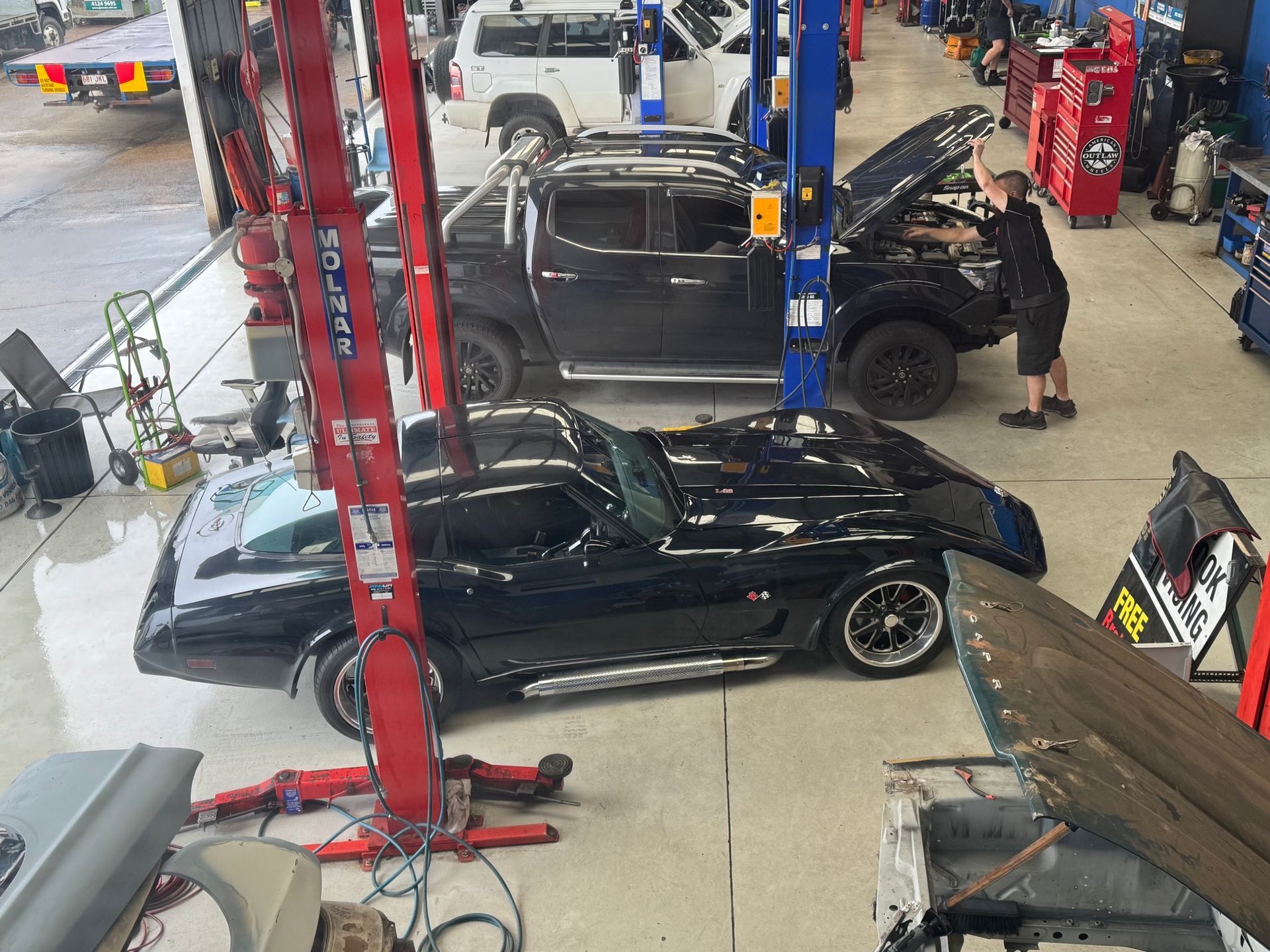 A black Corvette in a mechanic shop, a person working on a truck with its hood open — Pialba Brake Clutch & Steering in Pialba, QLD