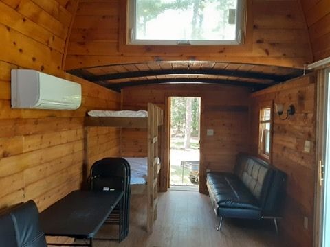 A wooden cabin with a couch , table , chairs and bunk beds.