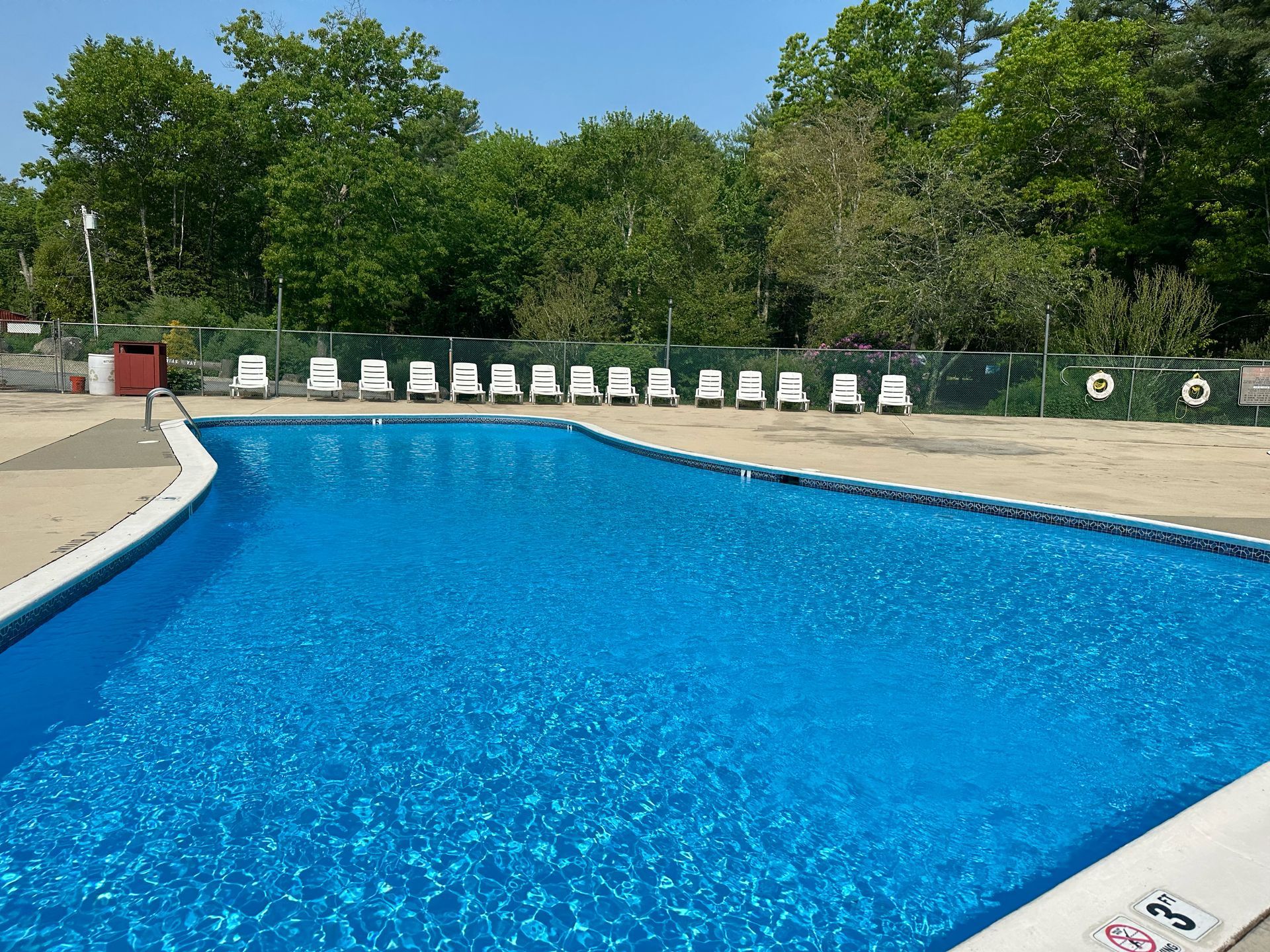 A large swimming pool surrounded by chairs and trees on a sunny day