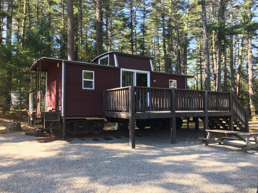 A small red house with a large deck in the middle of a forest.