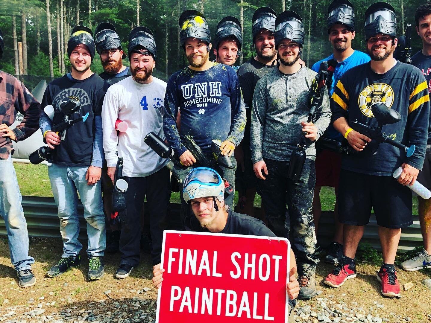 A group of men are posing for a picture with a sign that says final shot paintball.