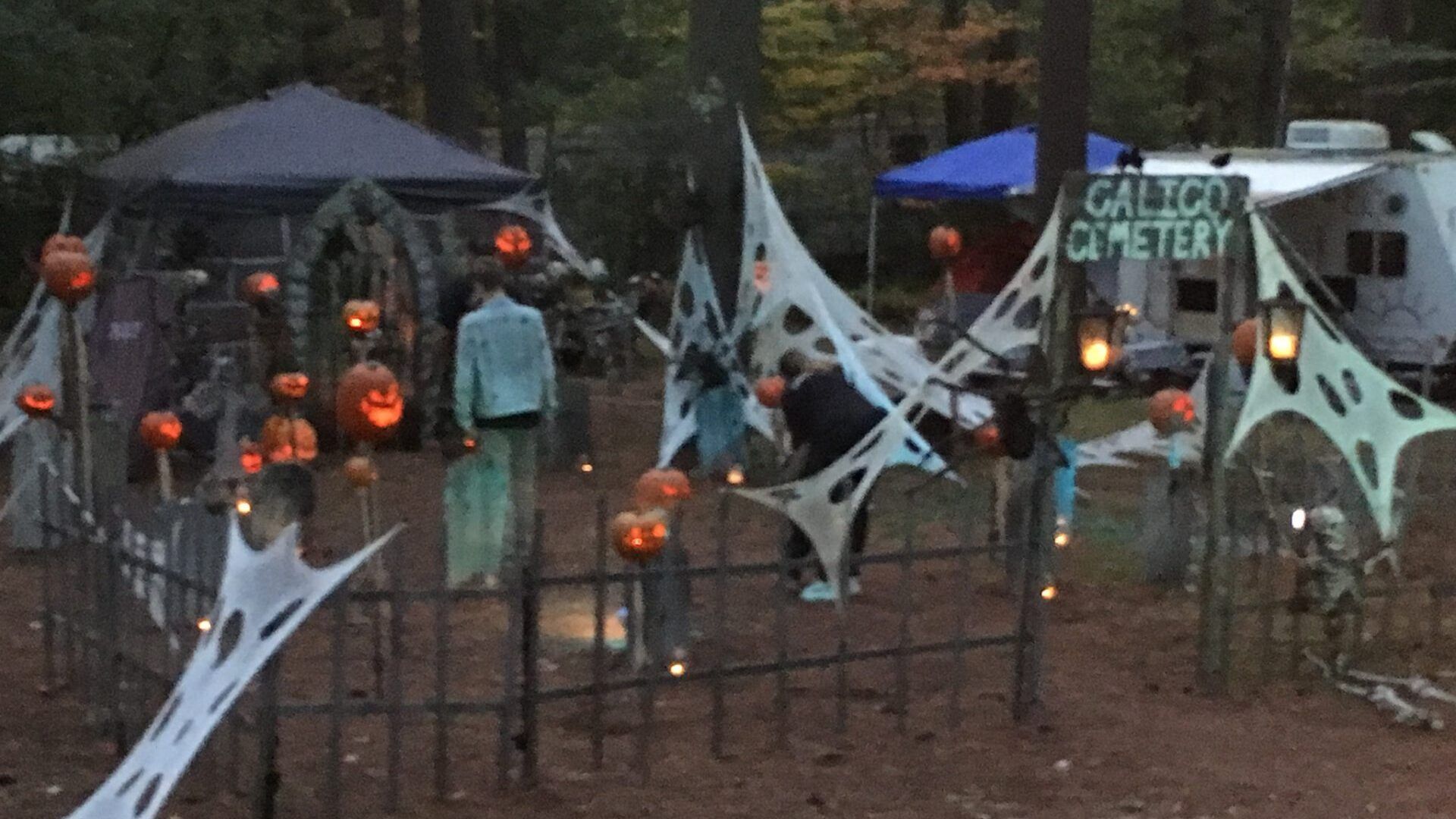 A cemetery is decorated for halloween with pumpkins and spider webs.