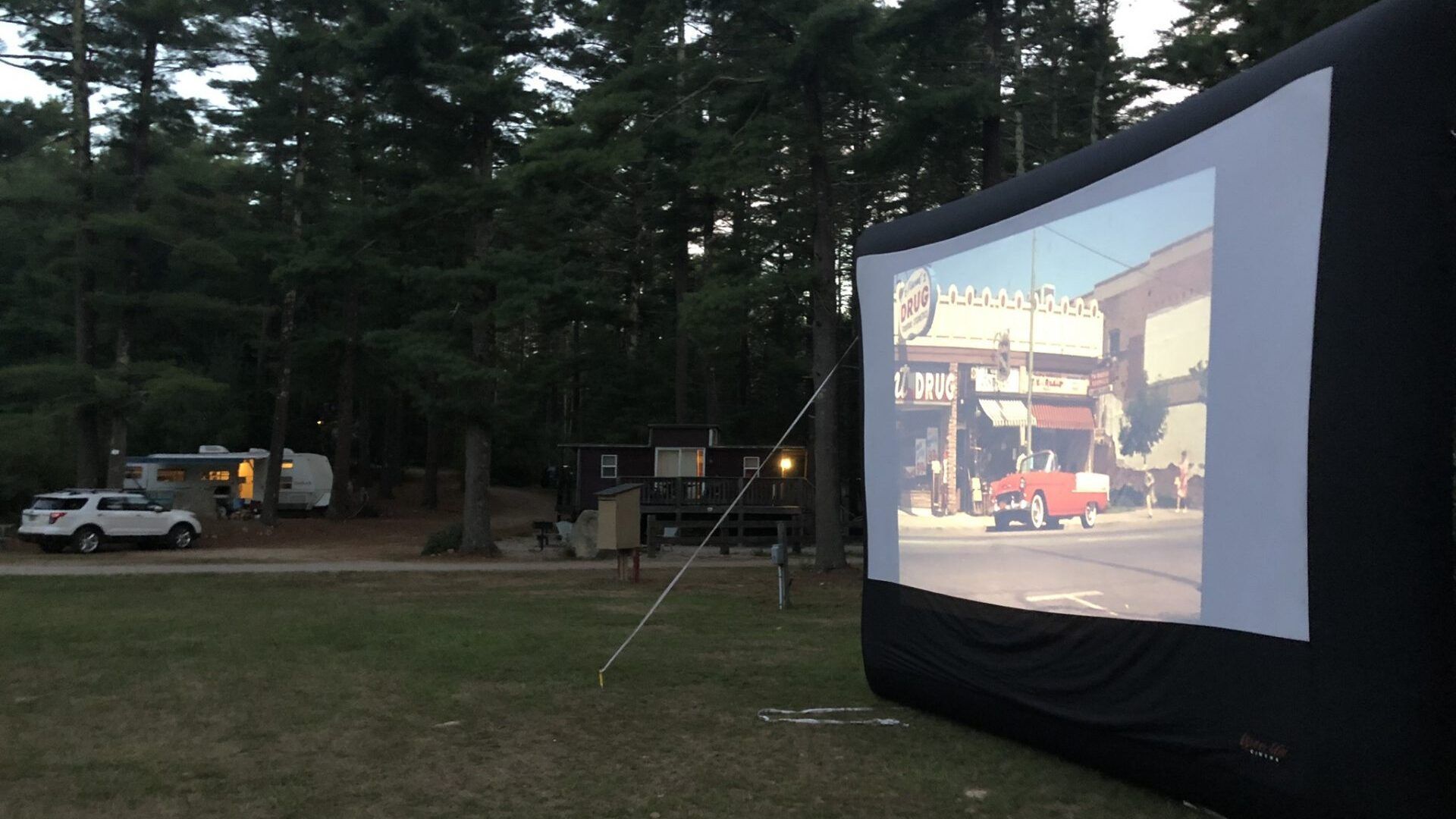A large inflatable screen is displaying a movie in a park
