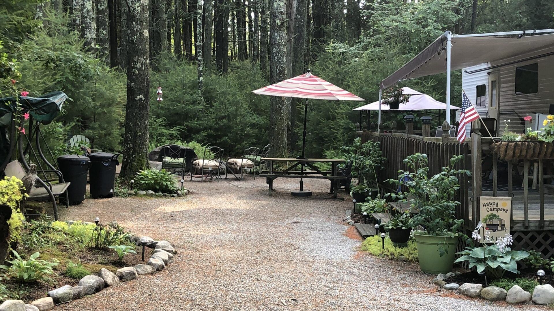 A rv parked in the woods with umbrellas and a picnic table.