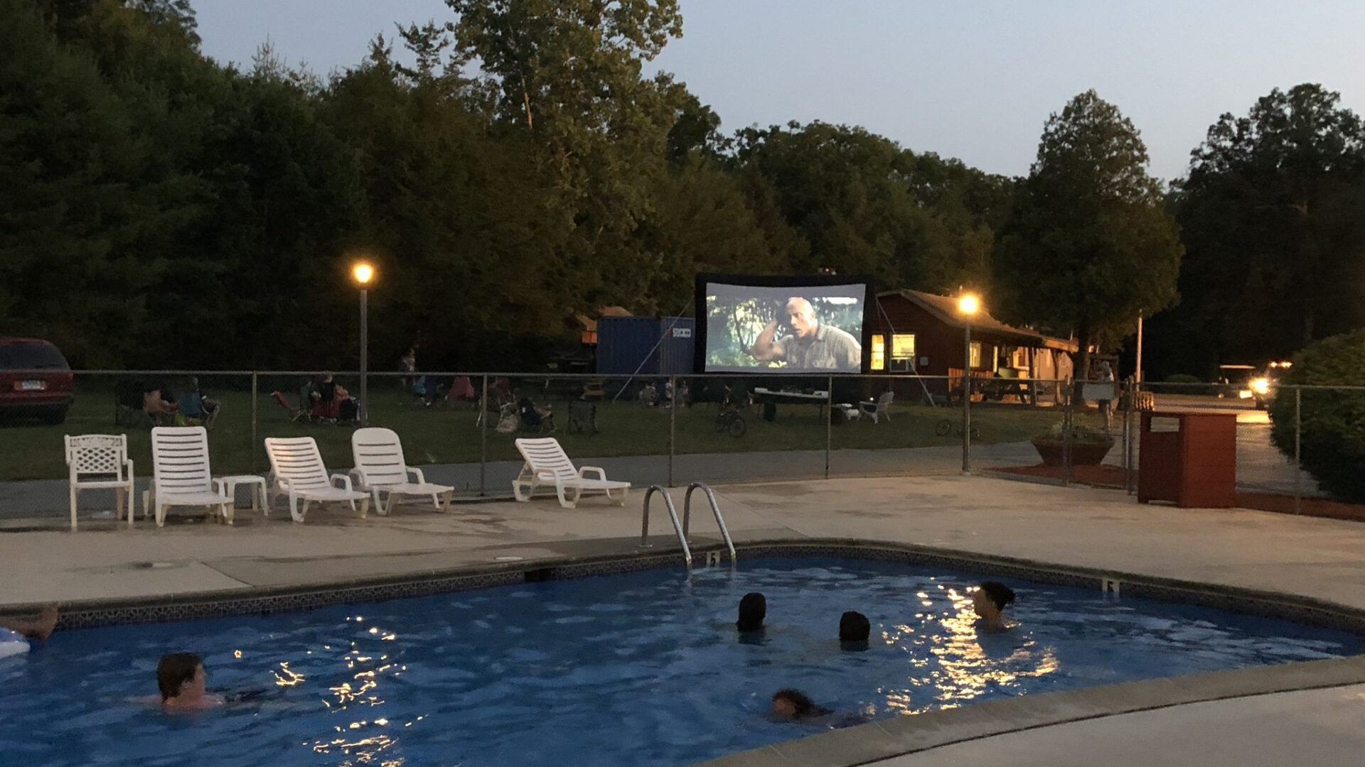 People are swimming in a pool in front of a large screen.