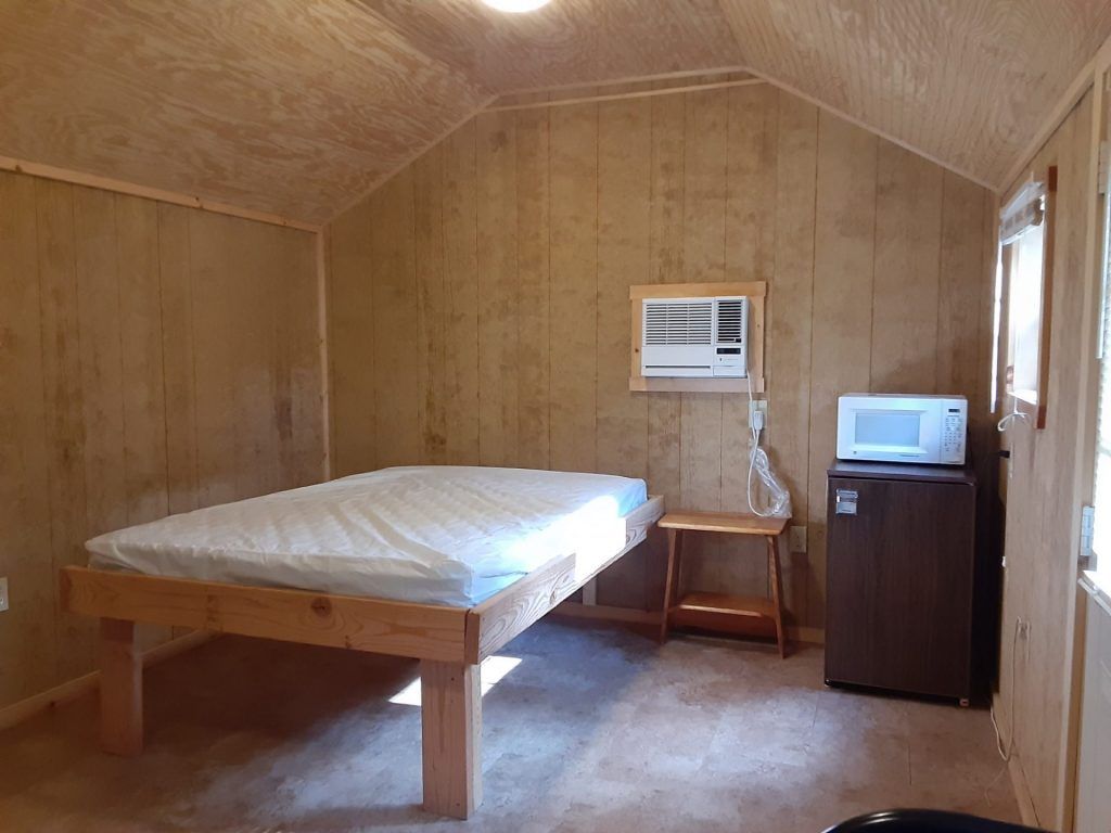 A bedroom with a bed , refrigerator , microwave and air conditioner.