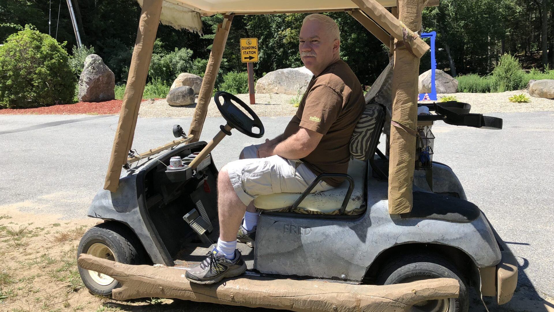 A man is sitting in a golf cart made to look like a caveman hut.