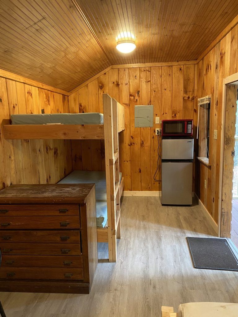 A room with bunk beds , a refrigerator , a microwave and a dresser.