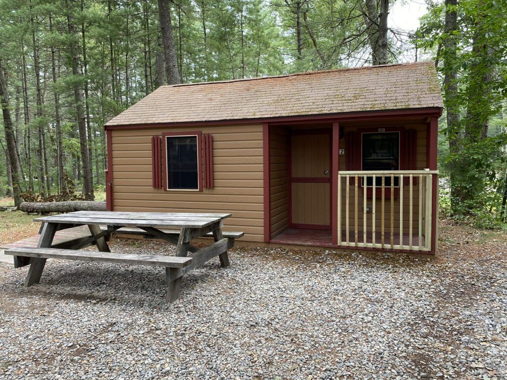 A small cabin with a picnic table in front of it in the woods.