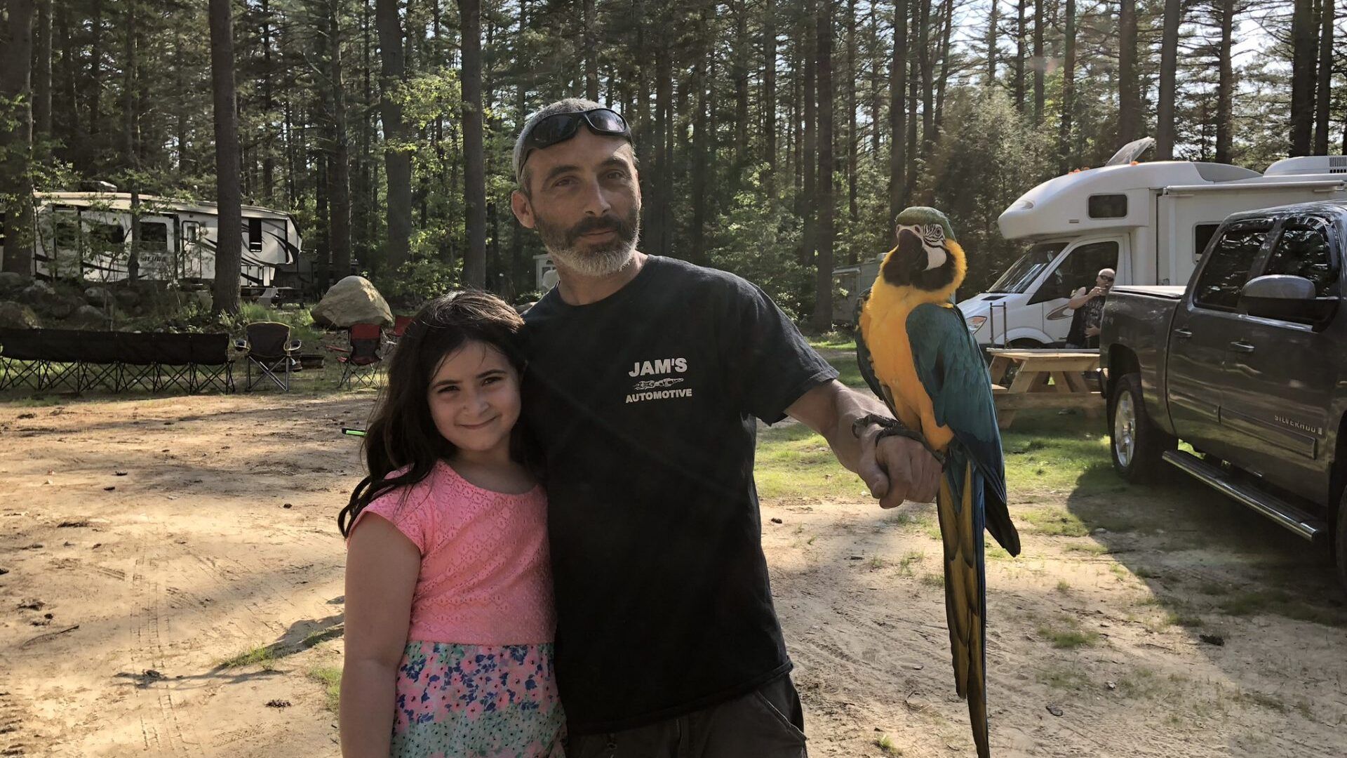 A man and a little girl are standing next to a parrot.