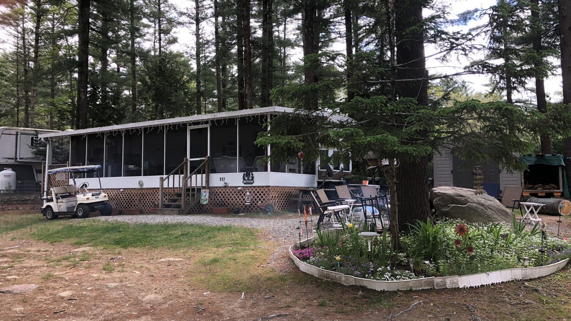 A mobile home in the middle of a forest with a golf cart parked in front of it.