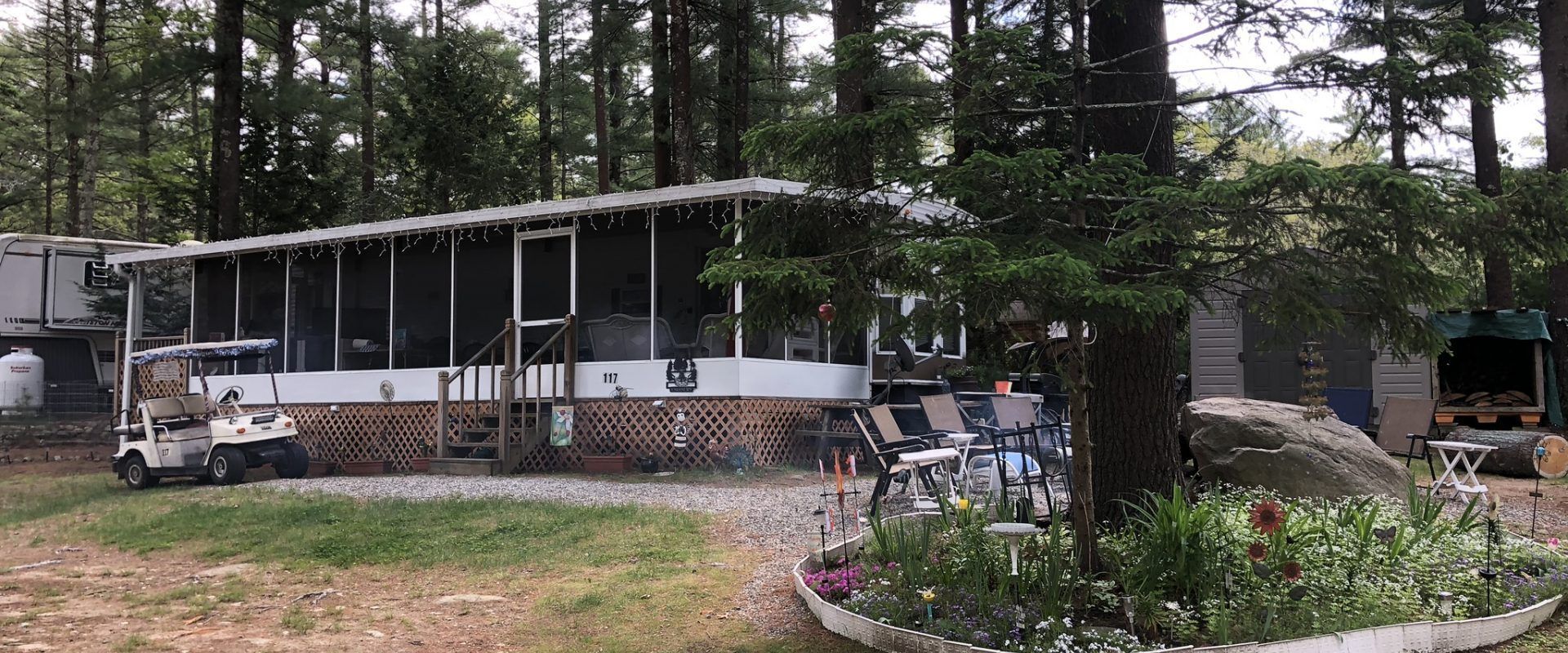 A mobile home with a screened in porch is surrounded by trees.