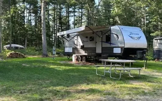 A rv is parked in a grassy area with a picnic table.
